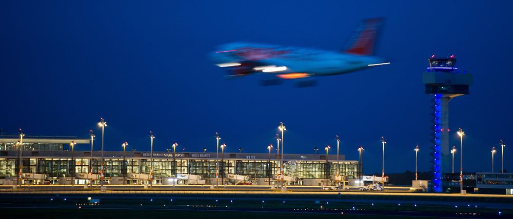 Ein Passagierflugzeug landet neben dem hell erleuchteten Berlin Brandenburg Airport Willy Brandt (BER).