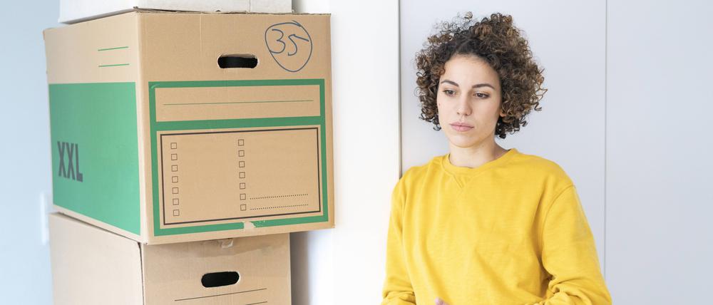 Eine nachdenklich wirkende Frau steht in einer Wohnung neben gepackten Kisten. 