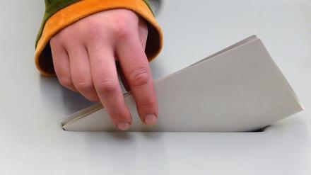 Eine Hand steckt einen Stimmzettel in die Wahlurne. 