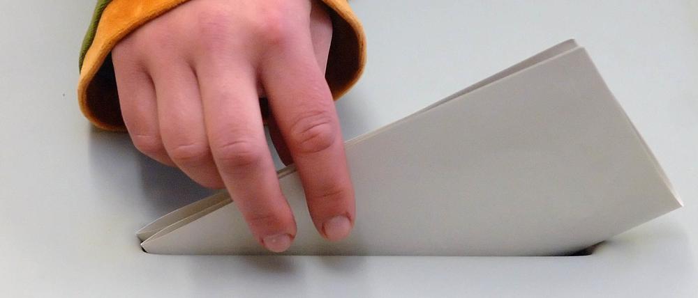 Eine Hand steckt einen Stimmzettel in die Wahlurne.