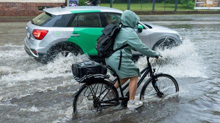 Eine Radfahrerin und ein Auto fahren im Schritttempo durch die überflutete Zeppelinstraße in Potsdam.