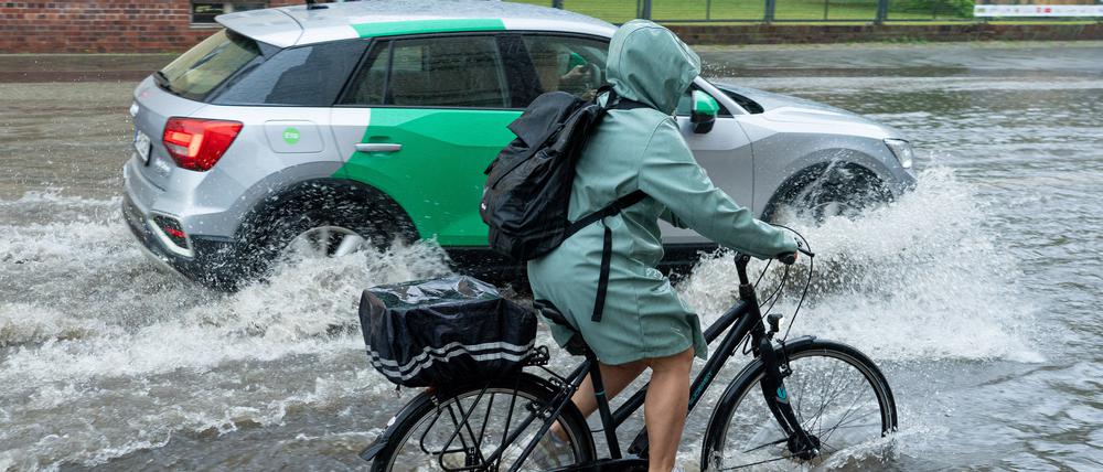Eine Radfahrerin und ein Auto fahren im Schritttempo durch die überflutete Zeppelinstraße in Potsdam.