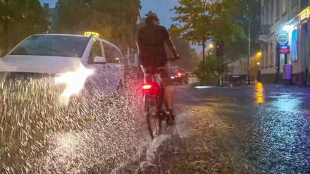 Baden-Württemberg, Freiburg im Breisgau: Ein Fahrradfahrer und ein Auto fahren über eine vom Regen überschwemmte Straße (Archivbild vom 24.08.2023).
