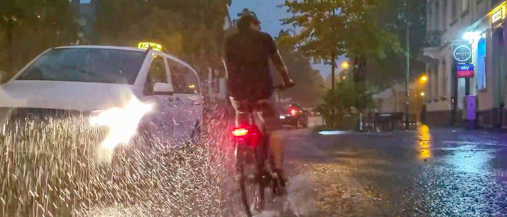 Baden-Württemberg, Freiburg im Breisgau: Ein Fahrradfahrer und ein Auto fahren über eine vom Regen überschwemmte Straße (Archivbild vom 24.08.2023).