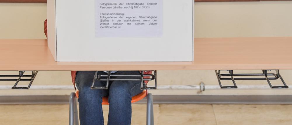 Eine Wählerin sitzt im Wahllokal in einer Grundschule hinter einer Wahlkabine und füllt ihre Stimmzettel für die Europawahl und die Kommunalwahl aus.