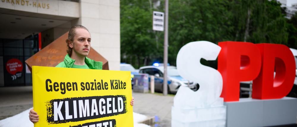 Ein Aktivist hält bei einer Protestaktion der Umweltschutz-Organisation Greenpeace vor der SPD-Zentrale ein Schild mit der Aufschrift „Gegen soziale Kälte - Klimageld jetzt!“. Greenpeace-Aktivisten haben vor der SPD-Zentrale in Kreuzberg etwa eine Tonne Eis ausgeschüttet und ein gefrorenes „S“ vom SPD-Schriftzug aufgestellt, um für die Einführung des Klimagelds zu demonstrieren.