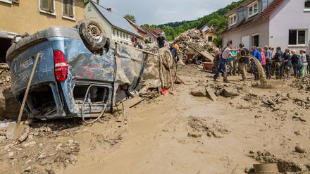 Helfer bilden eine Menschenkette, um möglichst viel Schlamm mit Eimern aus einem Haus im Ort zu bekommen, während davor ein Auto auf dem Dach liegt.