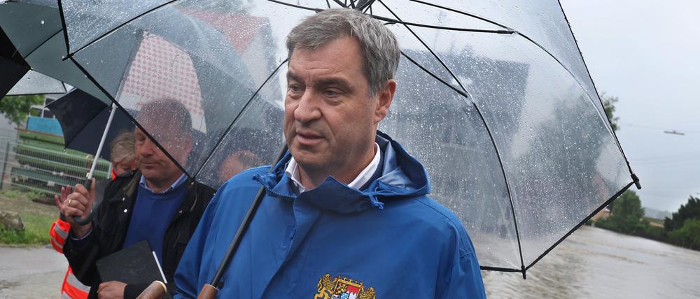 Markus Söder (CSU), bayerischer Ministerpräsident steht, umringt von Journalisten, am Rande einer überfluteten Straße. 