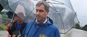 Markus Söder (CSU), bayerischer Ministerpräsident steht, umringt von Journalisten, am Rande einer überfluteten Straße. 
