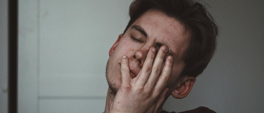 Ein Mann mit niedergeschlagenem Gesichtsausdruck und geschlossenen Augen hält sich eine Hand vors Gesicht