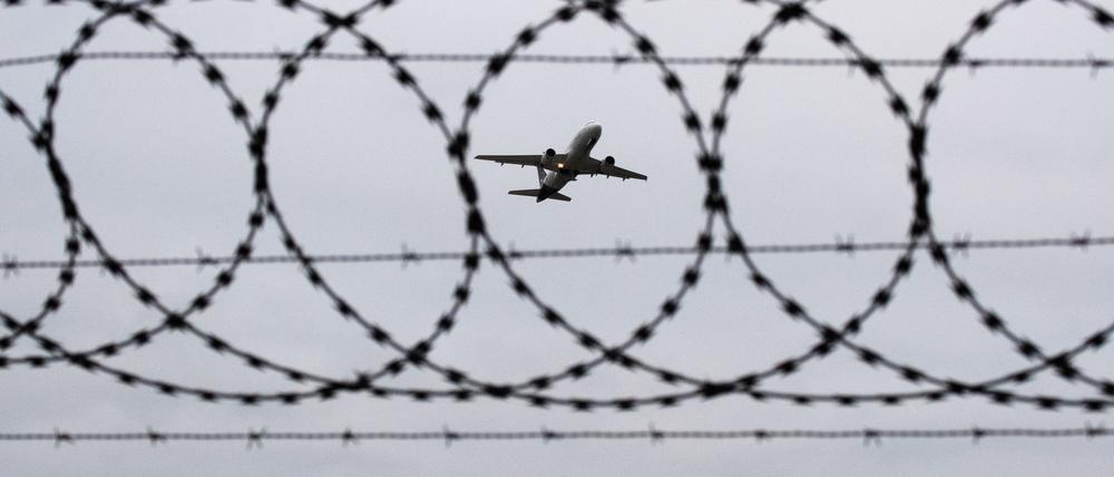 Ein Flugzeug startet – fotografiert durch Stacheldraht am Flughafenzaun (Symbolbild).