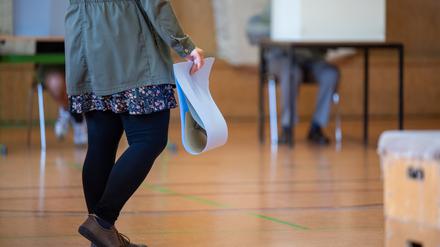 Eine wahlberechtigte Frau wartet in einem Wahllokal mit ihren Stimmzetteln in der Hand auf die Stimmabgabe.