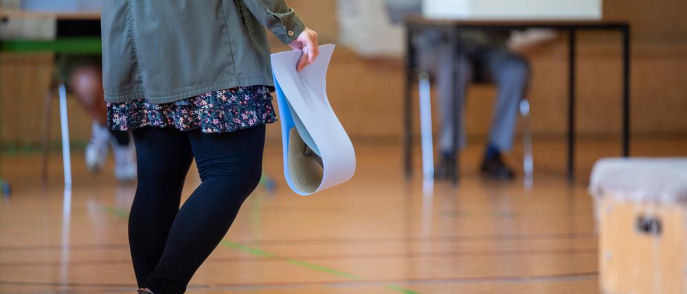 Eine wahlberechtigte Frau wartet in einem Wahllokal mit ihren Stimmzetteln in der Hand auf die Stimmabgabe.