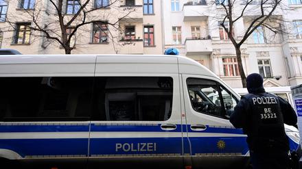 Ein Polizeibeamter steht neben einem Polizeifahrzeug, das vor einem Gebäude im Berliner Stadtteil Neukölln geparkt ist.