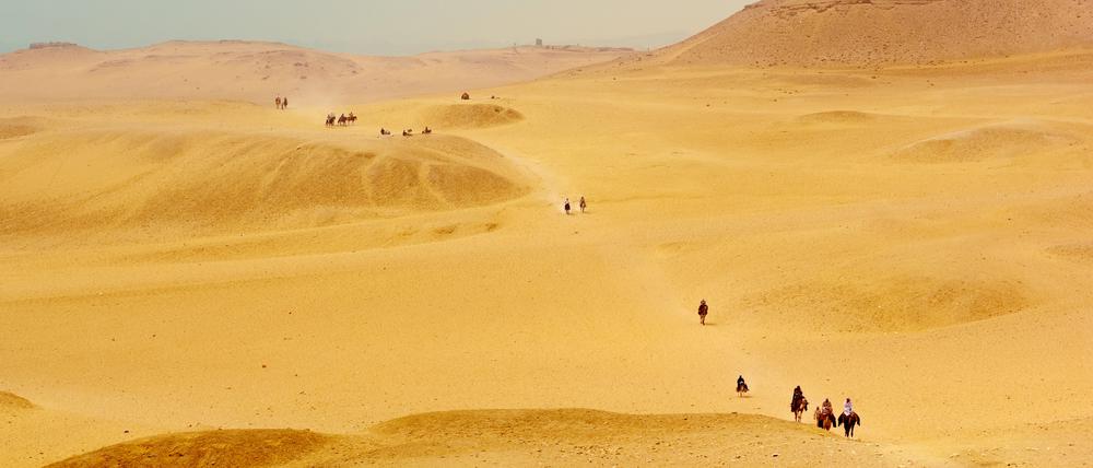 Menschen reiten in der Wüste von Ägypten bei flirrender Hitze auf Pferden.