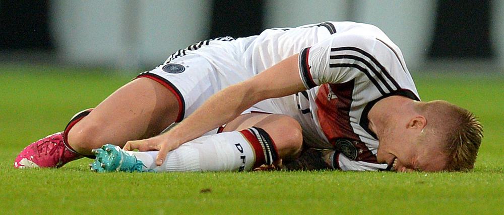 Fußballspieler Marco Reus liegt am Boden und hält sich das linke Sprunggelenk.