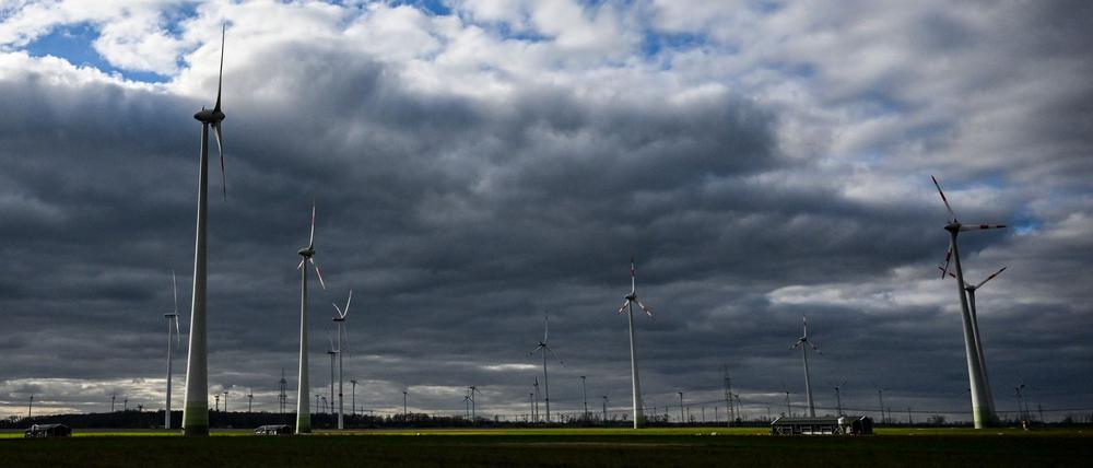 Windräder werden bei wolkigem Himmel kurzzeitig von der tiefstehenden Sonne beleuchtet.