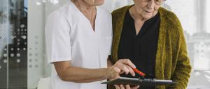 Eine medizinische Angestellte hilft einer älteren Patientin beim Ausfüllen eines Dokuments.