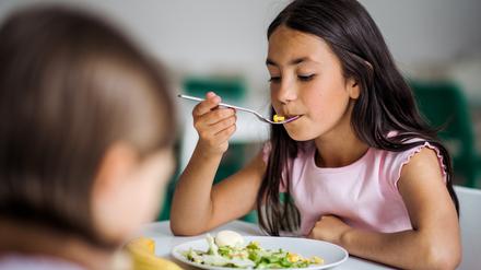 Two small school girlas in canteen, eating lunch.