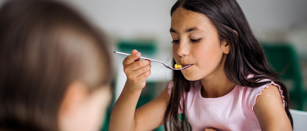 Two small school girlas in canteen, eating lunch.