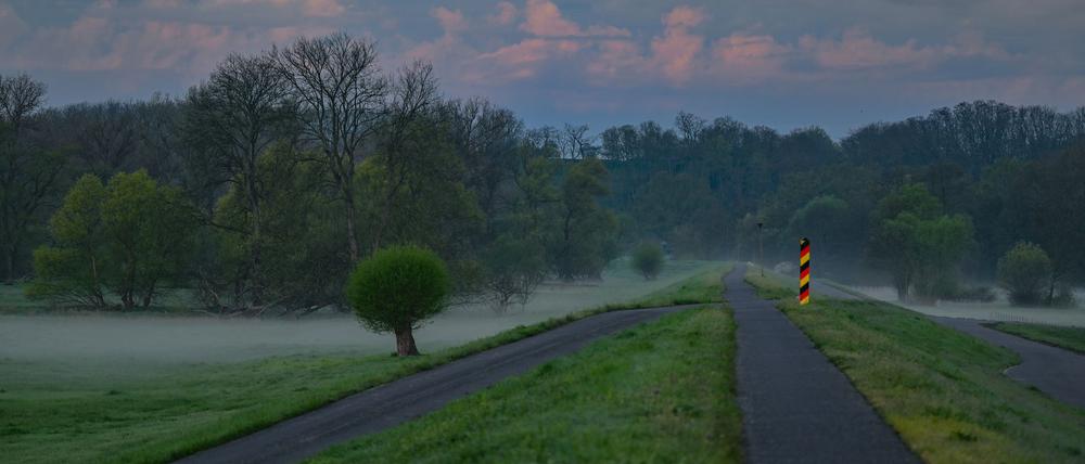 Der Sonnenaufgang scheint auf Wolken über dem Oder-Neiße-Radweg am Deich nahe dem deutsch-polnischen Grenzfluss Oder.