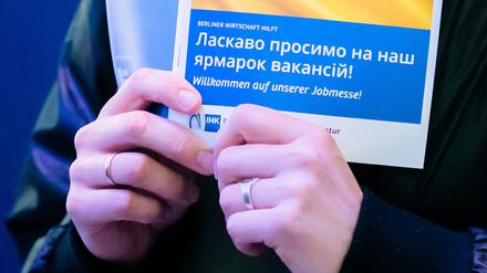 Eine Frau hält bei einer Jobmesse für ukrainische Geflüchtete den Messeplan mit der ukrainischen Flagge. (Symbolbild)
