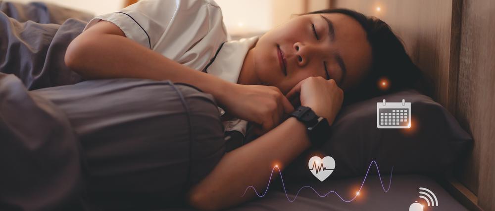 Eine Frau liegt im Bett und hat eine Smartwatch um, die ihren Schlaf überwacht.
