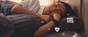 Eine Frau liegt im Bett und hat eine Smartwatch um, die ihren Schlaf überwacht.