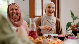 Muslimische Frauen und ein Mann sitzen beim Essen gemeinsam an einem Tisch und lachen. 