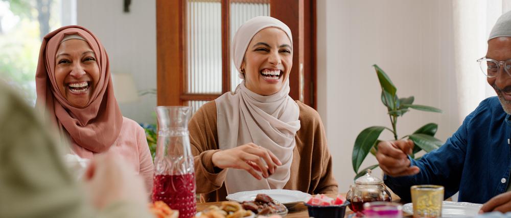 Muslimische Frauen und ein Mann sitzen beim Essen gemeinsam an einem Tisch und lachen. 