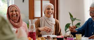 Muslimische Frauen und ein Mann sitzen beim Essen gemeinsam an einem Tisch und lachen. 