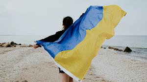 Eine junge Frau läuft mit ausgebreiteten Armen, die Flagge der Ukraine haltend, einen Strand entlang