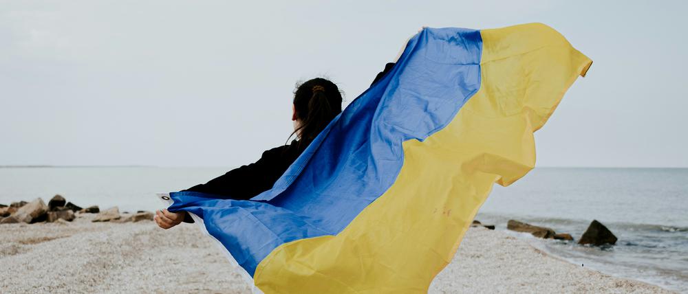 Eine junge Frau läuft mit ausgebreiteten Armen, die Flagge der Ukraine haltend, einen Strand entlang