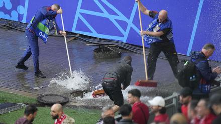 Mitarbeiter beseitigen Wasser, nachdem sie während eines starken Regens vor dem Spiel einen Kanaldeckel entfernt haben. 