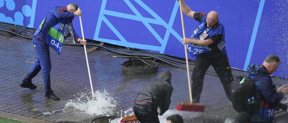 Mitarbeiter beseitigen Wasser, nachdem sie während eines starken Regens vor dem Spiel einen Kanaldeckel entfernt haben. 