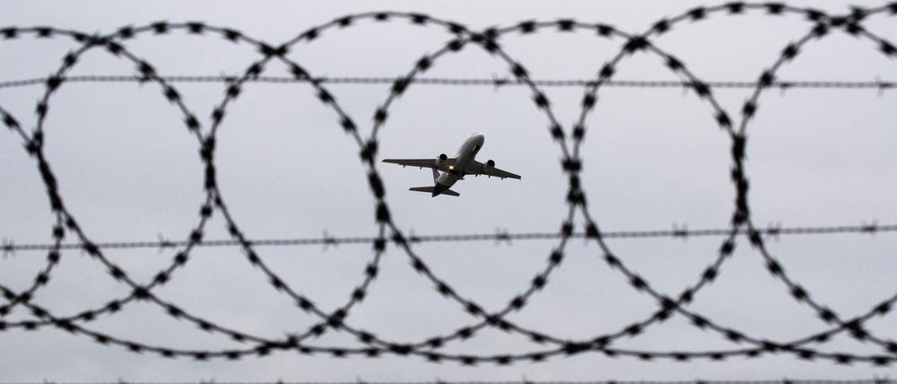 Ein Flugzeug startet – fotografiert durch Stacheldraht am Flughafenzaun.
