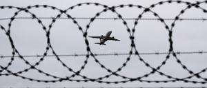 Ein Flugzeug startet – fotografiert durch Stacheldraht am Flughafenzaun.
