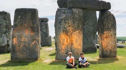 Demonstranten von „Just Stop Oil“ sitzen vor dem Steinmonument Stonehenge, das sie zuvor mit orangener Farbe besprüht haben.