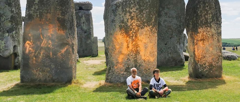 Demonstranten von „Just Stop Oil“ sitzen vor dem Steinmonument Stonehenge, das sie zuvor mit orangener Farbe besprüht haben.