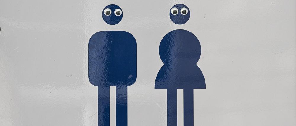 Ein Schild Mann und Frau mit einem Pfeil weist im Park Charlottenburg auf die Toiletten hin. Die Piktogramme sind mit Augen beklebt. 