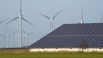 Windenergieanlagen stehen neben einer Halle mit Photovoltaik-Anlagen auf dem Dach (Symbolbild).
