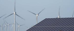 Windenergieanlagen stehen neben einer Halle mit Photovoltaik-Anlagen auf dem Dach (Symbolbild).