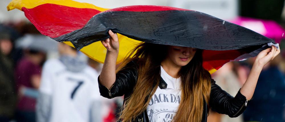 Eine Frau läuft am 26.06.2014 in Berlin beim „Public Viewing“ am Brandenburger Tor während des WM-Fußballspiels Deutschland - USA durch den strömenden Regen. 