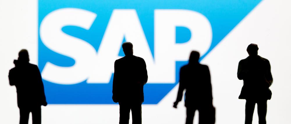 Kleine Plastikfiguren vor dem Logo des DAX-Unternehmens SAP. In Deutschland streicht der Konzern zahlreiche Stellen.