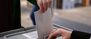 Ein Wähler steckt bei einer Wahl seinen Wahlzettel in eine Urne.