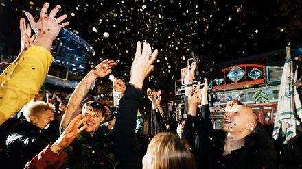 A group of friends celebrating throwing confetti in the air on the dance floor, having fun at an open air nightclub.