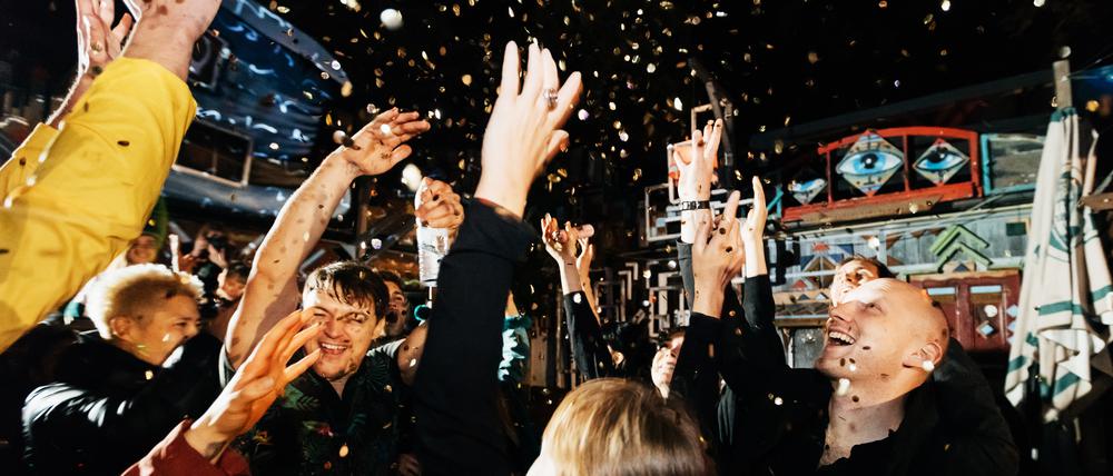 A group of friends celebrating throwing confetti in the air on the dance floor, having fun at an open air nightclub.