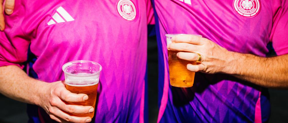 Zwei Männer im pinken EM-Trikot liegen sich mit Bier in der Hand in den Armen.