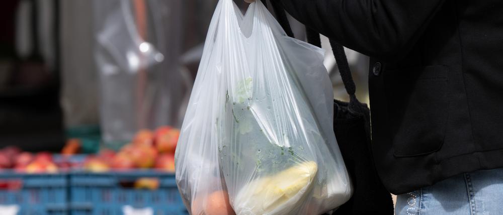 Eine Frau trägt ihre Einkäufe in Plastiktüten auf einen Wochenmarkt. 