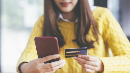 Eine Frau hält Smartphone in der einen und Kreditkarte in der anderen Hand.